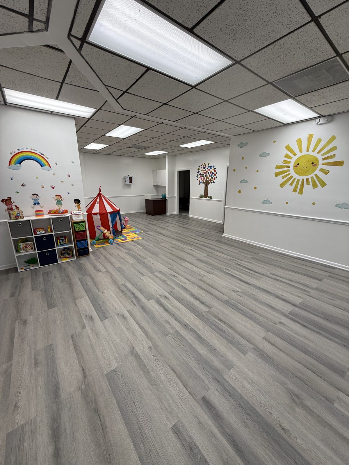 Bright playroom at Caring Hands PediPec with a rainbow and sun mural, toy shelves and a play tent